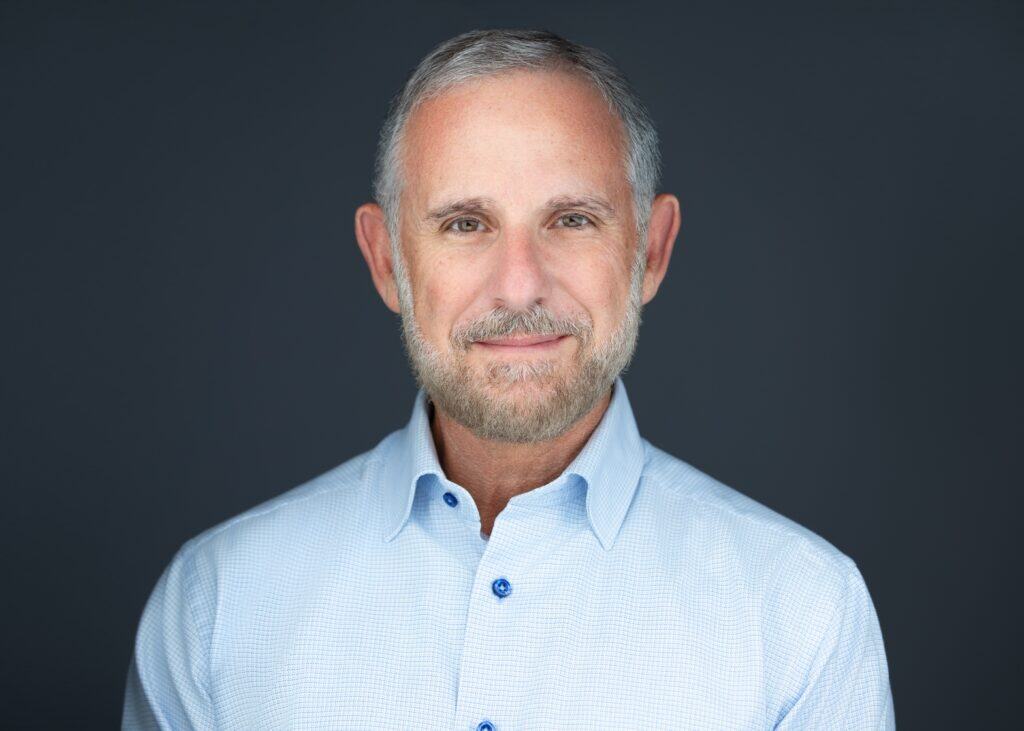 Senior man with gray hair and beard wearing a light blue shirt, professional portrait.